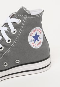Grijze canvas hoge sneakers met witte veters, een zwart-wit gestreepte zool en een ronde logo met een blauwe ster.