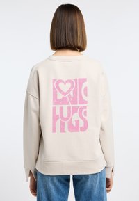 Beige sweatshirt met een opvallende roze grafiek met de tekst "LOVE HUGS" op de achterkant; gemaakt van zachte stof met een ontspannen pasvorm en splitmouwen.