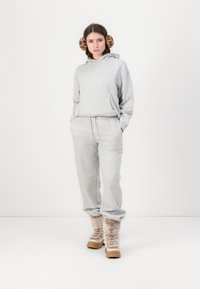 Set din bluză și pantaloni de trening gri din țesătură moale, cu glugă și talie elastică, completat de cizme pufoase bej cu o talpă robustă.
