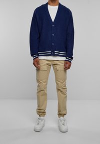 Marineblauw geribbelde cardigan met een V-hals, vijf knopen en witte gestreepte manchetten, gecombineerd met beige cargobroek en witte sneakers.