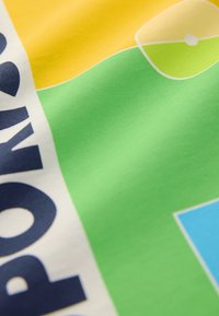 Daugiaspalvė medžiaga su geltonomis, žaliomis ir baltomis dalimis. Akcentuojamas ryškus juodas tekstas ir mėlynas stačiakampis elementas. Lygi tekstūra.