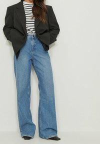 Blazer noir oversize, chemise rayée blanche et marine, et jean en denim bleu à jambes larges. Texture lisse avec une usure subtile sur le jean.