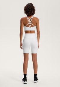 Sutien sport alb cu bretele încrucișate, asociat cu pantaloni scurți moto albi cu talie înaltă. Textură netedă; design minimalist; îmbrăc�ăminte sport.
