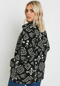 Giacca in pile nera con motivi geometrici bianchi e colletto. Presenta una vestibilità comoda e maniche lunghe.