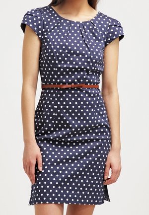 Robe marine avec des pois blancs, manches courtes, col plissé, taille cintrée et une ceinture marron. Tissu lisse avec un léger éclat.
