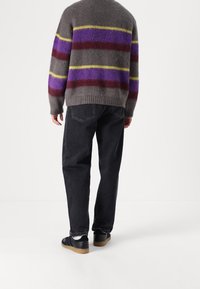 Maglione grigio con strisce viola, gialle e bordeaux, caratterizzato da una texture morbida. Abbinato a jeans neri e sneakers nere con suola in gomma.