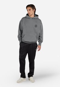 Grijze pullover hoodie met een voorzak en logobelemmering, gecombineerd met zwarte sportbroeken en lichtgekleurde sneakers.