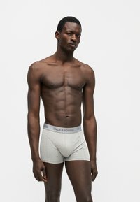 Μαύρος άνδρας μοντέλο, όρθιος, φοράει ανοιχτό γκρι μποξεράκια με ελαστική μέση "JACK & JONES", σε λευκό απλό φόντο.