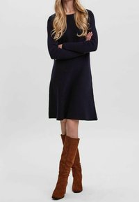 Robe bleu marine à manches longues avec une coupe décontractée, dotée d'un col rond. Associée à des bottes en daim marron jusqu'aux genoux avec un léger talon.