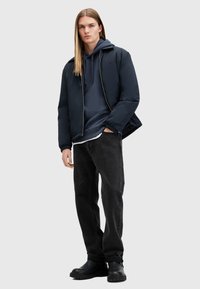 Navy puffer jacket over a dark hoodie, paired with black jeans and chunky black boots. Smooth fabric and ribbed cuffs, minimal detailing.