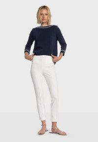 Haut en maille marine avec bordure blanche, assorti à un pantalon blanc sur mesure avec poches latérales et lignes épurées. Des sandales argentées complètent le look.