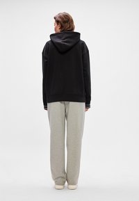 Mustat hupparit, joissa on roikkuvat olkapäät, yhdistettynä vaaleanharmaisiin verkkareihin. Molemmat vaatekappaleet on valmistettu pehmeästä, rennosta kankaasta.