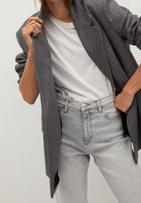 Szary żebrowany blazer o strukturalnym kroju, noszony na białym t-shircie. W zestawieniu z jasnoszarymi dżinsami, podkreślającymi fakturę i dopasowanie.