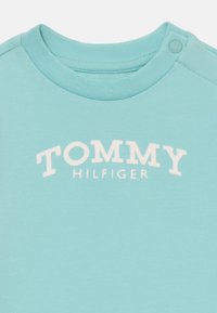 Svetlomodré tričko s okrúhlym výstrihom, s bielym logom "TOMMY HILFIGER" na prednej strane a cvokom na pleci.