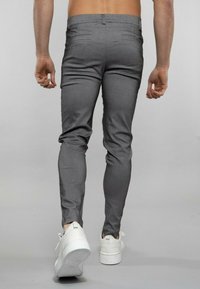 Pantalons slim gris avec une texture lisse, dotés d'une taille mi-haute, de deux poches arrière, et associés à des baskets blanches.