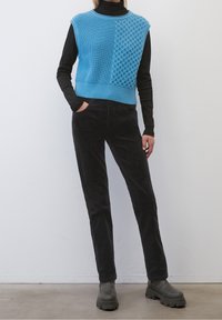 Sininen neulottu crop-top, jossa on tekstuurikuvioita, yhdistettynä mustiin korduroypantoihin ja raskaisiin tummiin saapikkaisiin. Taustalla neutraali tausta.
