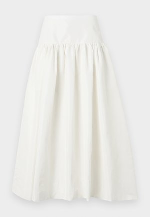 Vrouw draagt een witte korte mouwen gebreide top met een veterkraag en een lange witte rok met hoge taille en crème puntige hakken.