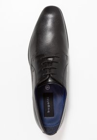 Chaussure habillée en cuir noir avec une finition texturée, bout rond et fermeture à lacets. L'intérieur présente une doublure bleue et une étiquette de marque.