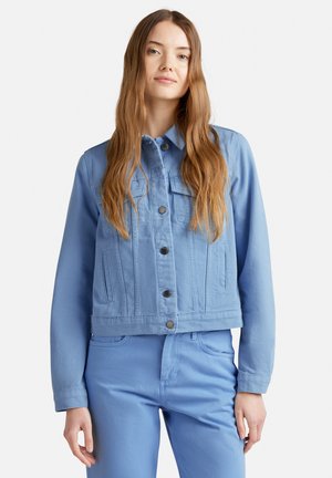 Chaqueta de mezclilla azul clara recortada con un cierre frontal de botones, dos bolsillos en el pecho y costuras visibles. Presenta mangas largas y un cuello puntiagudo.