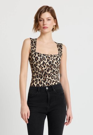 Femme portant un haut sans manches à motif léopard avec un décolleté carré et un jean noir taille haute, debout devant un fond clair uni.