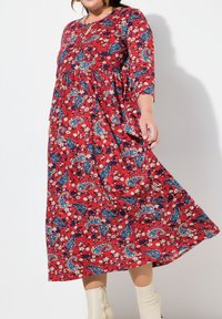 Długa czerwona sukienka z niebieskim paisley i białymi kwiatowymi wzorami, z okrągłym dekoltem, rękawami o długości trzy czwarte oraz swobodną sylwetką.