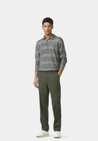 Poloshirt met lange mouwen in grijze en zwarte horizontale strepen, gecombineerd met donkergroene broek en witte sneakers, wat een casual look laat zien.