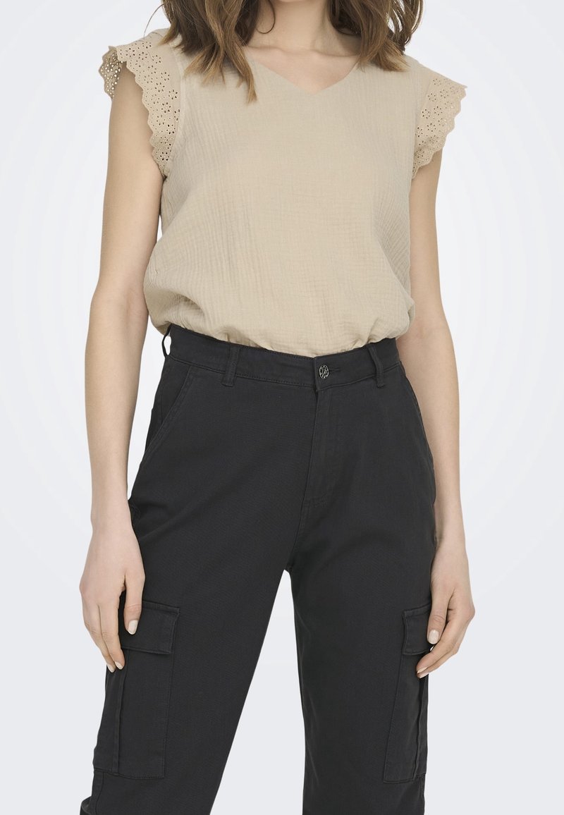Haut beige texturé à col en V avec des manches courtes ornées de dentelle, associé à un pantalon cargo noir avec poches latérales et fermeture à boutons.
