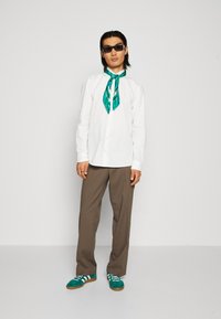 Witte button-up shirt, groene zijden sjaal, bruine brede broek en teal sneakers met witte strepen; moderne, casual outfit.