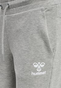 Zbliżenie szarych dresów z przednią kieszenią, ściągaczem w pasie i białym logo Hummel na udzie.