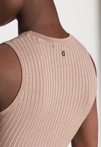 Haut sans manches côtelé beige, avec un col rond et un petit logo noir à l'arrière. Texture douce avec une silhouette ajustée.