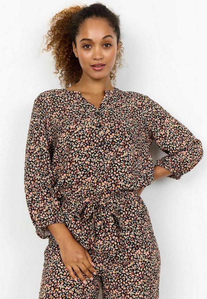 Blusa con stampa floreale su sfondo nero, caratterizzata da scollatura a V e maniche lunghe arrotolate. Realizzata in tessuto leggero con una vestibilità ampia.