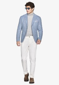 Blazer azzurro chiaro a spina di pesce con rever, dolcevita grigio a maglia, pantaloni bianchi e scarpe marroni, accentuato da occhiali da sole scuri.