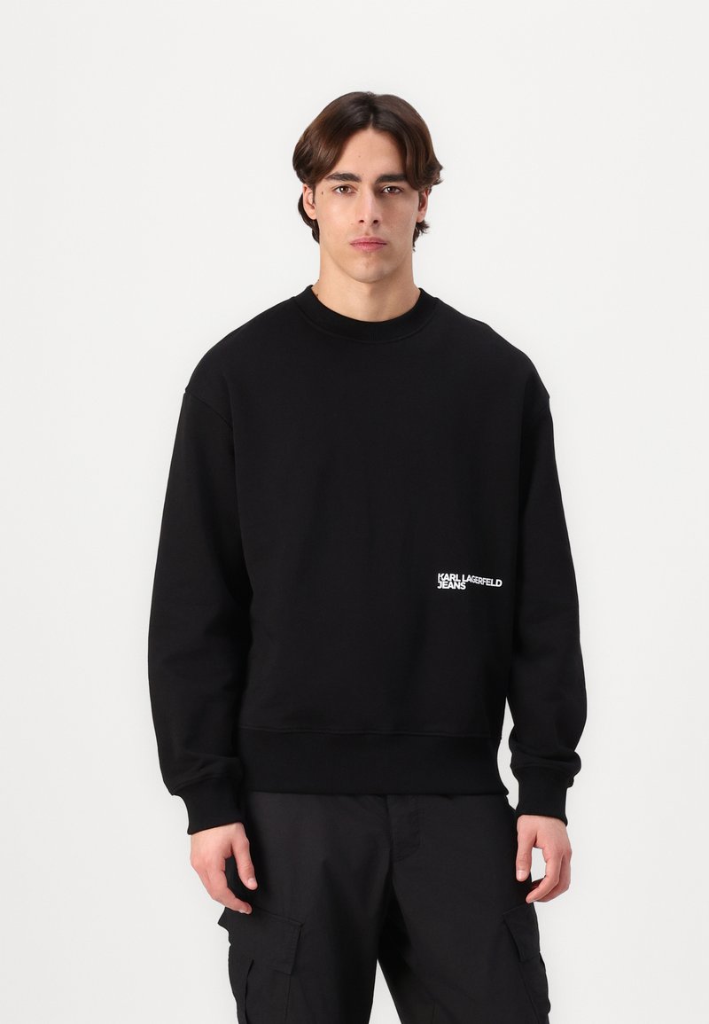Schwarzer Sweatshirt mit Rundhalsausschnitt, gerippten Bündchen und Saum. Enthält ein weißes bedrucktes Logo auf der linken Seite. Hergestellt aus weichem, strukturiertem Stoff.