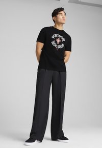 Sort t-shirt med "PORTUGAL" grafisk design og nationalemblem foran, parret med løstsiddende sorte bukser og sorte sneakers.
