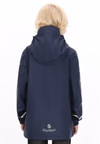 Jūras spēku nokrišņu jaka ar kapuci, elastīgiem aprocēm un auklu ap kaklu. Jakai ir logo tuvumā apakšmalai un atstarojoši akcenti uz piedurknēm.