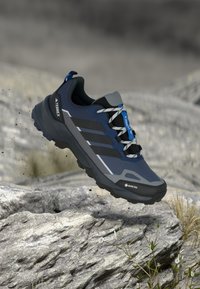 Πεζοπορικό παπούτσι GORE-TEX σε ναυτικό μπλε με γκρι τόνους, με ανάγλυφη επάνω επιφάνεια, μαύρα κορδόνια και ανθεκτική σόλα, σχεδιασμένο για σταθερότητα σε ανώμαλο έδαφος.