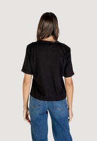 Czarny T-shirt z krótkim rękawem o luźnym kroju i podwiniętych mankietach, w połączeniu z jasnoniebieskimi spodniami o szerokich nogawkach. Tkanina wygląda na gładką i miękką.