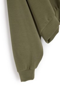 Oliwkowa bluza z szczotkowaną teksturą, luźnym krojem, opadającymi ramionami i szerokimi mankietami. Minimalistyczny design bez widocznych wzorów.