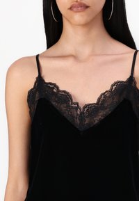 Black velvet camisole with lace trim along the neckline; thin adjustable straps; soft texture; fitted design highlighting the collarbone area.