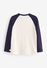 Majica z dolgimi rokavi, kremaste barve telesa in temno vijoličastimi raglan rokavi. Gladek bombažen material z okroglim izrezom in detajlom s stransko etiketo.