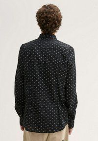 Chemise noire à manches longues, avec un petit motif de diamants dans des tons de gris, dotée d'un col classique.