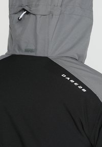 Zweifarbige graue und schwarze Kapuzenjacke mit weißem "DARE 2B" Logo im oberen Rückenbereich und verstellbarem Kordelzug an der Kapuze.