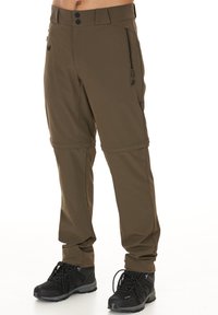 Bruine buitenbroek van flexibel materiaal met ritszakken, knopen op de tailleband en bijpassende zwarte wandelschoenen.