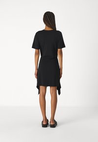 Schwarzes Kleid mit kurzen Ärmeln, asymmetrischem Saum und weicher Textur. Verfügt über eine lockere Passform und ein minimalistisches Design, ohne sichtbare Verzierungen.