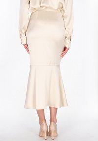 Falda de satén color crema con silueta de sirena, ajustada en las caderas y con vuelo en el dobladillo. Combinada con zapatos de tacón alto nude.