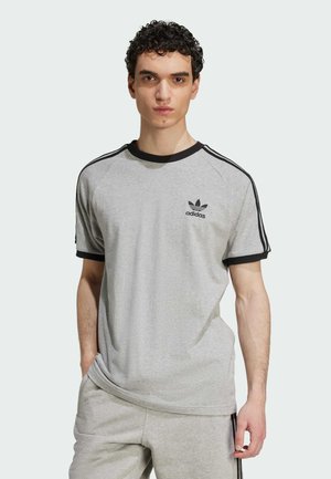 Grå kortärmad t-shirt med svarta detaljer och logotyp, med rund halsringning och raglanärmar. Tillverkad av bomull med en slät textur.
