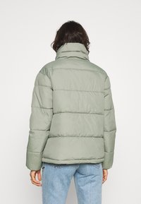 Ljusgrön pufferjacka med hög krage, med kviltade sektioner, långa ärmar och sidofickor med dragkedja, bärs över blå jeans.