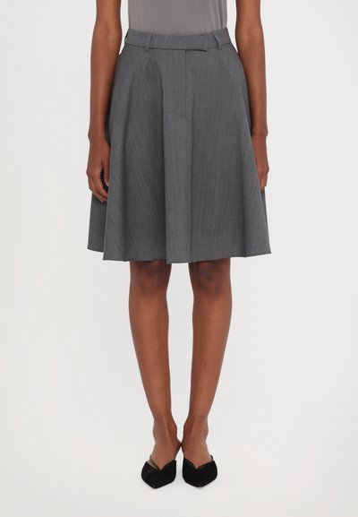 Falda gris plisada con cinturilla, hecha de tejido texturizado. Su forma acampanada llega justo por encima de la rodilla, combinada con tacones negros.
