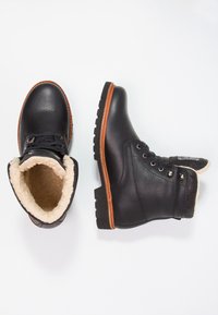 Botas de tobillo de cuero negro con forro de lana, punta redonda, suela de goma marrón y ojales de metal. Superficie texturizada y ribete marrón en contraste.