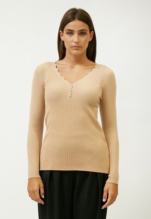 Top beige de manga larga con canalé y escote en V con bordes ondulados, con tres botones en la parte delantera. Textura suave con ligeros toques de brillo.